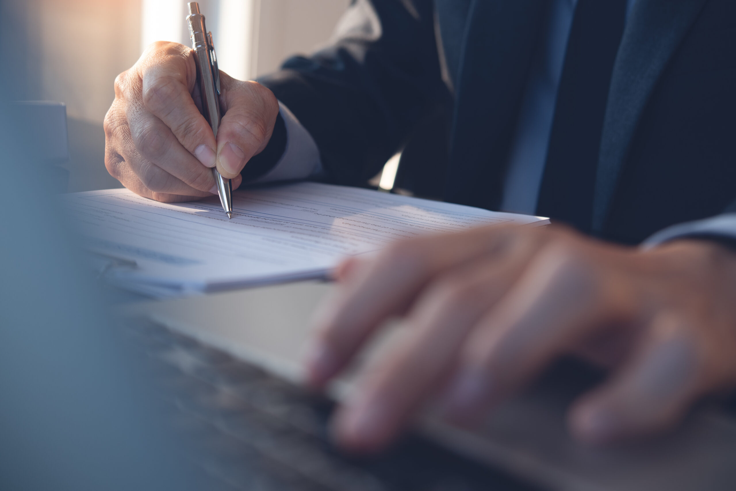 Deal concept. Businessman in black suit, executive manager signing business contract, partnership agreement document in modern office with laptop computer and digital tablet on table. close up